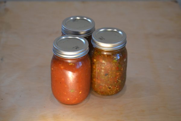 Three jars of homemade salsa on a wooden board
